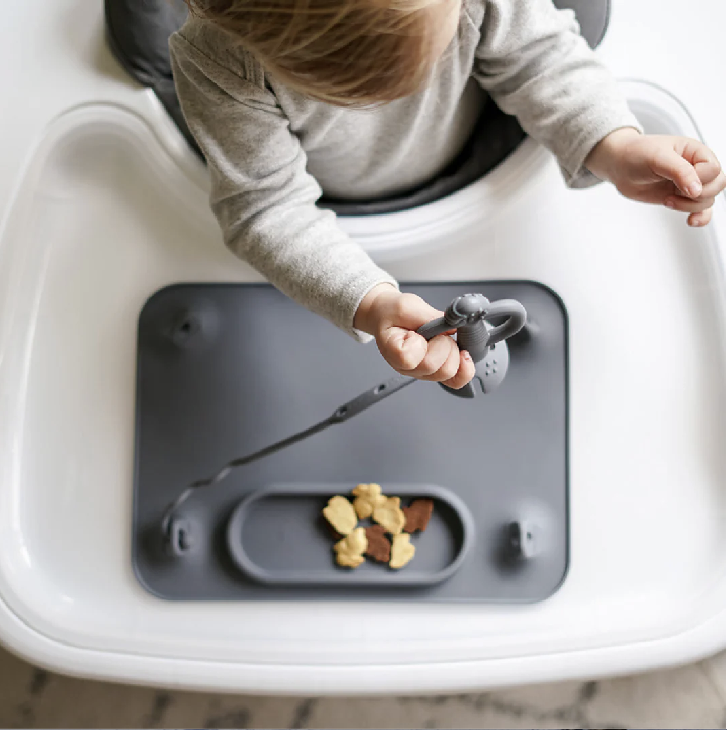 Baby in highchair using the Original Busy Baby Mat with tethered spoon