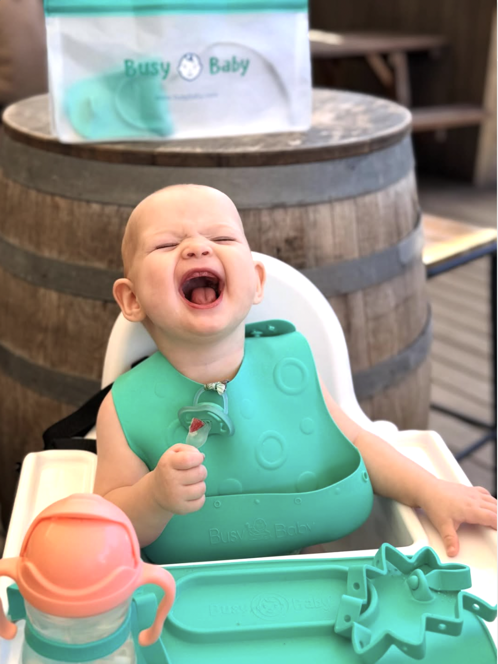 Baby laughing in highchair wearing Busy Baby bib